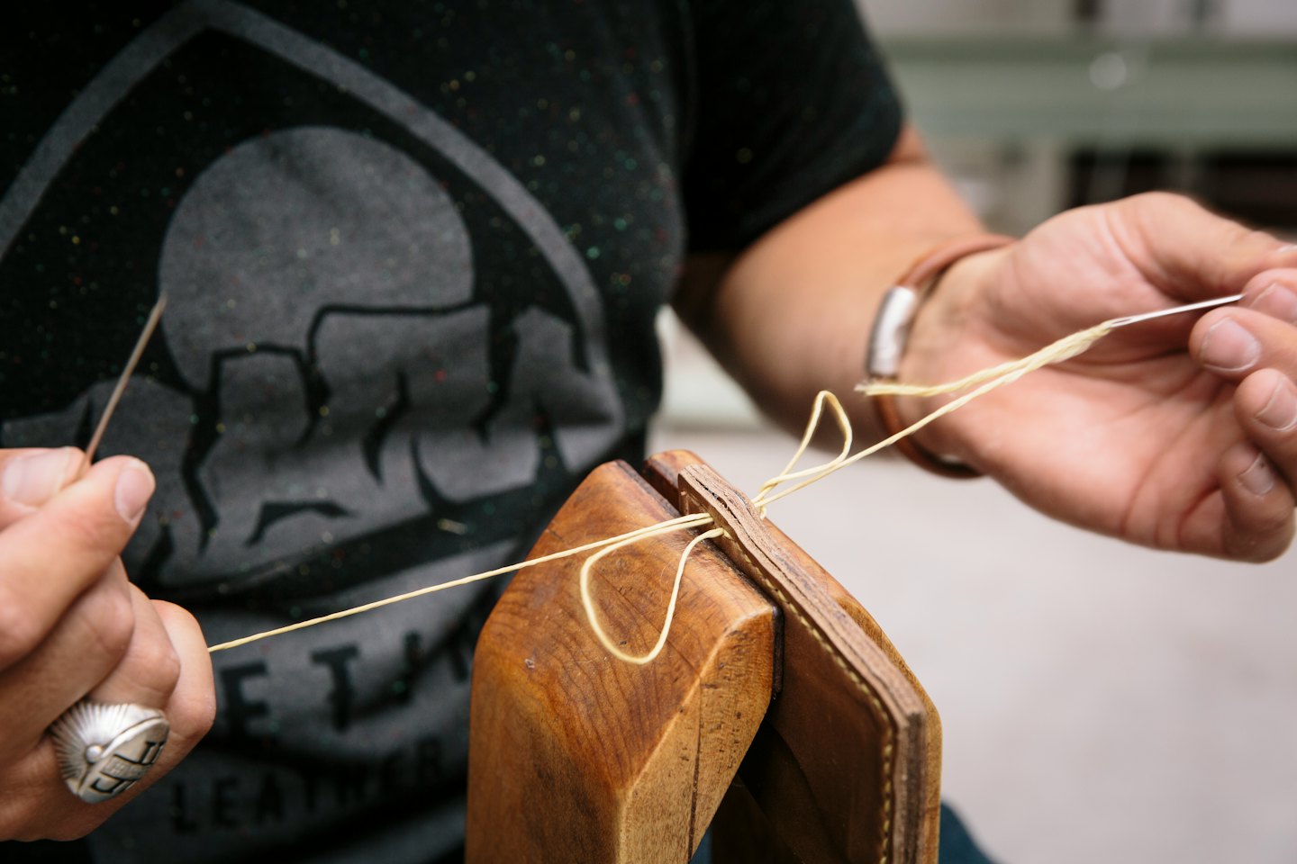 Hands stitching brown leather with light thread.