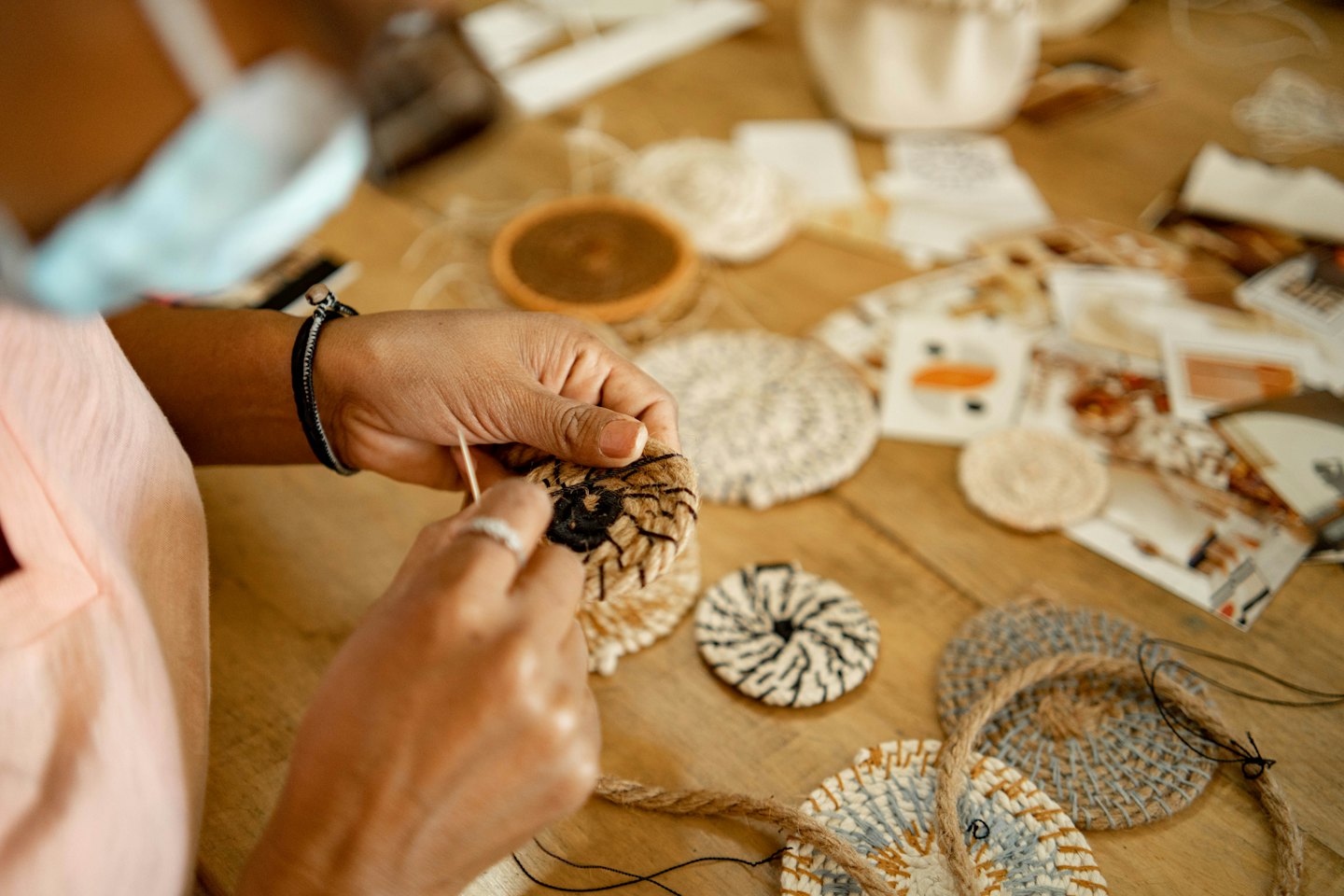Hands weaving a small circular object with natural fibers and a needle.