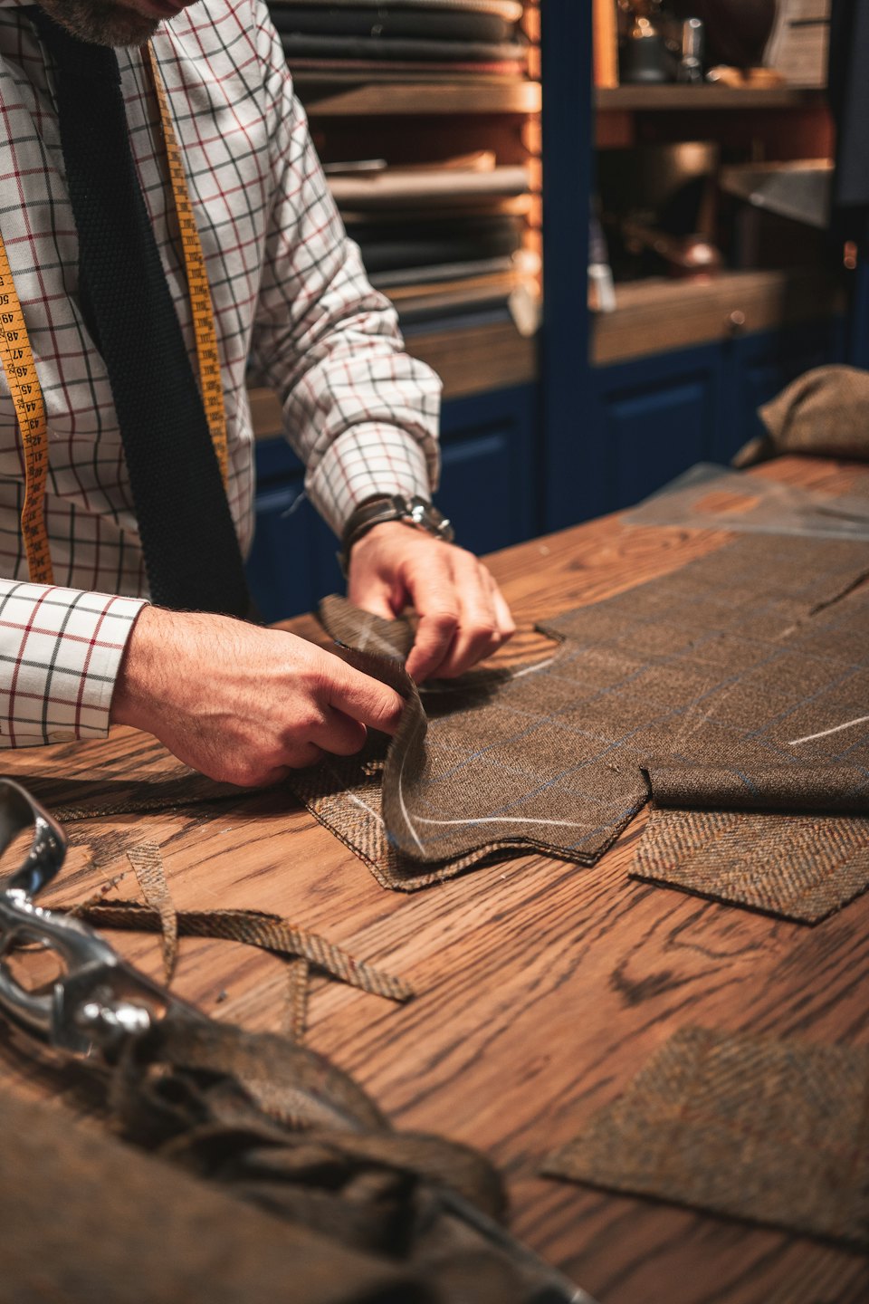 Tailor's hands work with tweed fabric on a workbench.