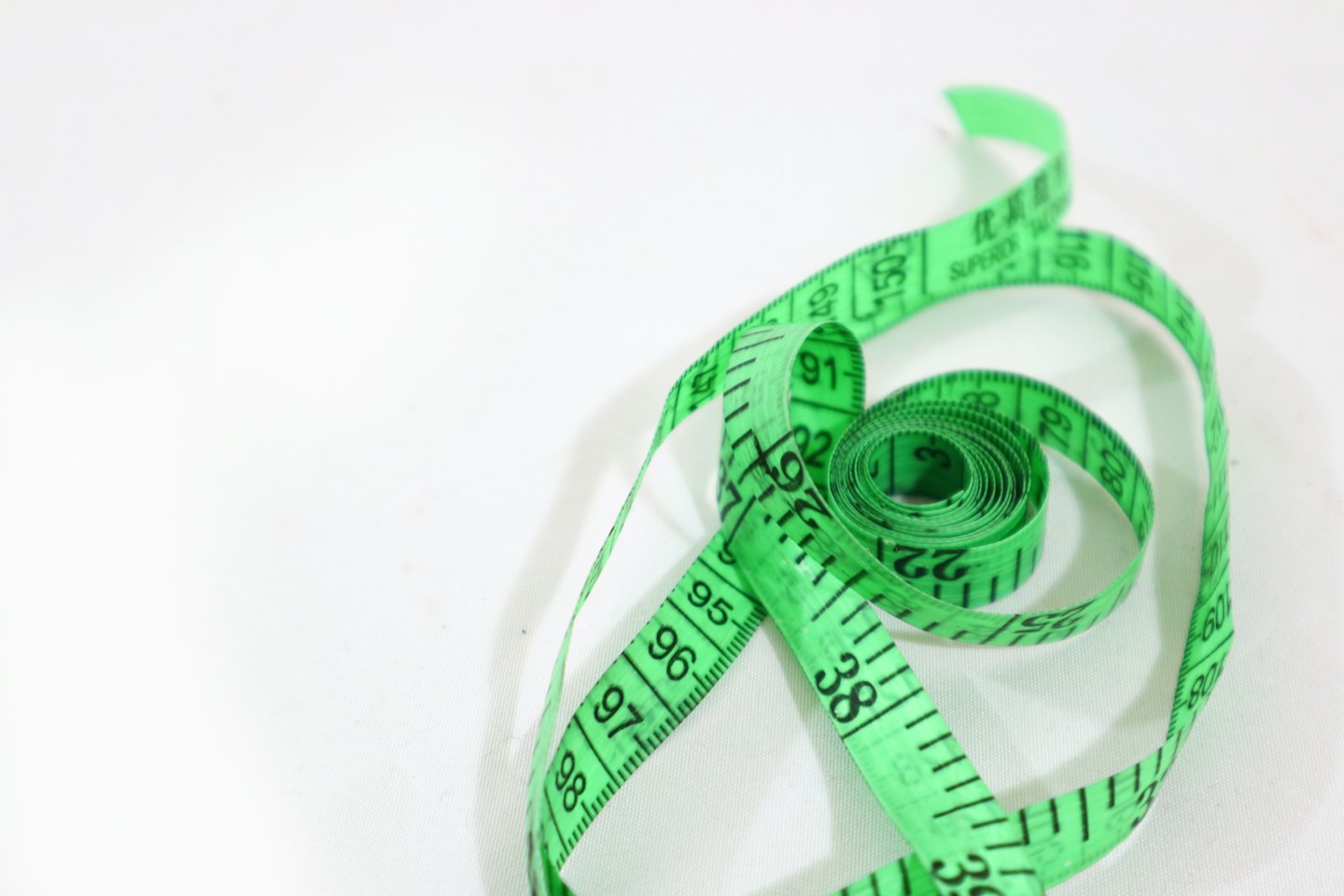 Green tailor's measuring tape unfurling on a white surface.