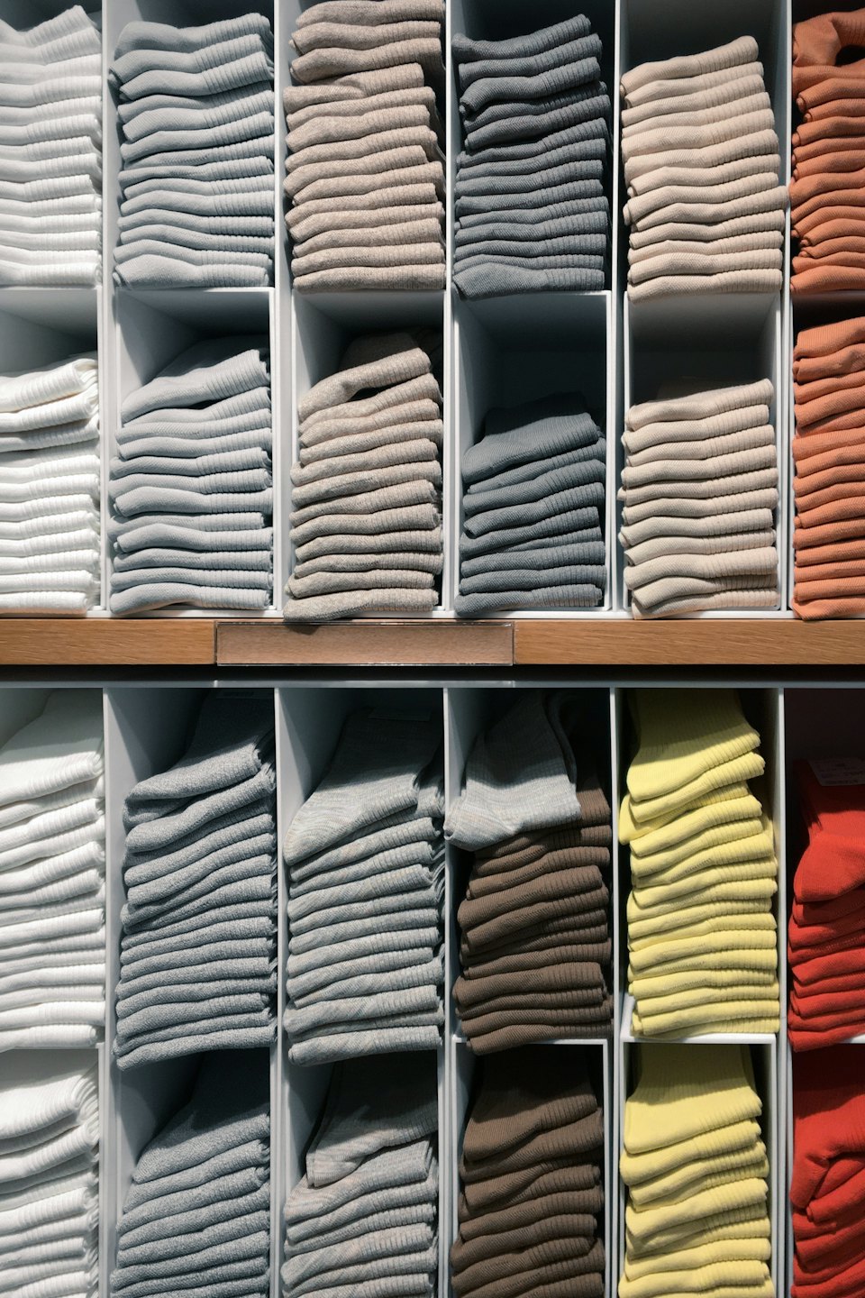 Neatly folded clothing arranged by color in white shelving compartments.