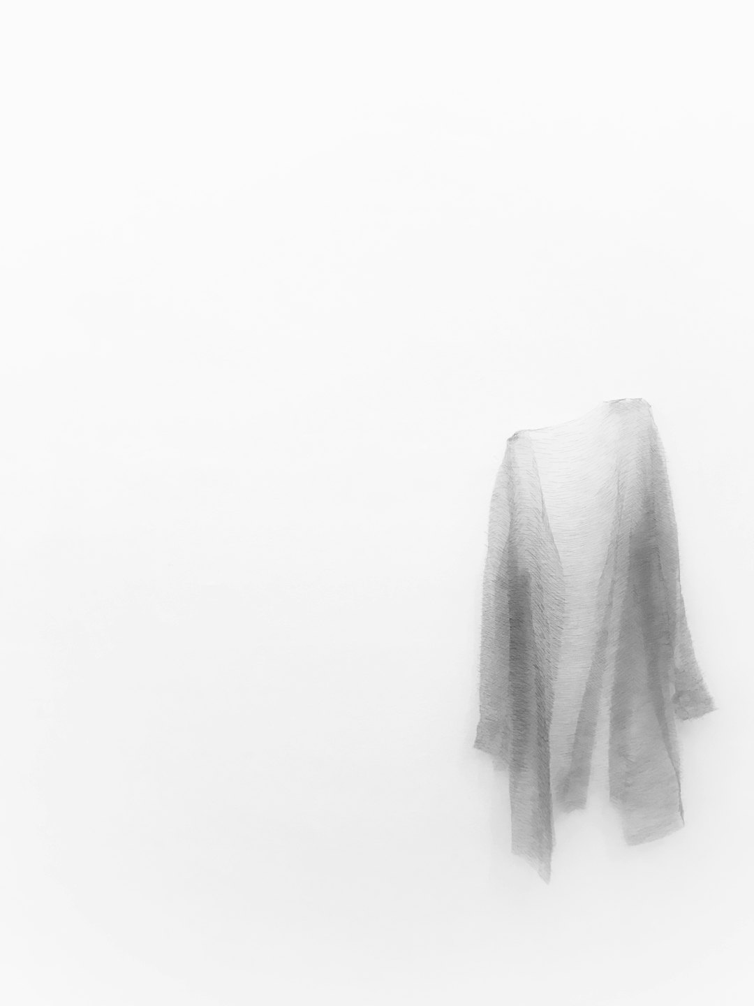 A textured grey shawl hangs against a white wall.